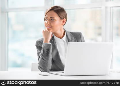 Thoughtful business woman holding chin while using laptop at work