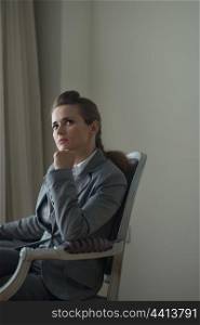 Thoughtful business woman sitting in chair in hotel room