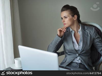 Thoughtful business woman working on laptop in hotel room