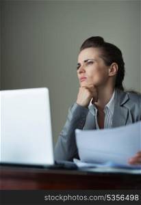 Thoughtful business woman working with documents and laptop at desk