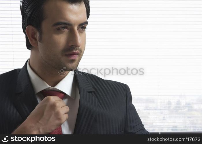Thoughtful businessman adjusting tie in office