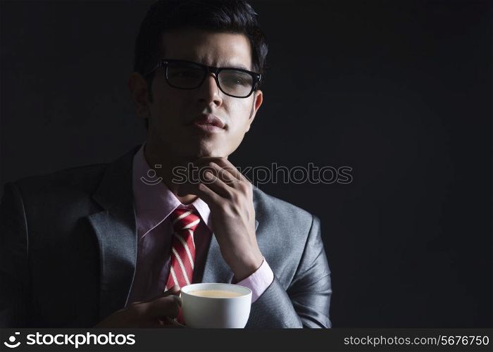 Thoughtful businessman holding coffee cup against black background