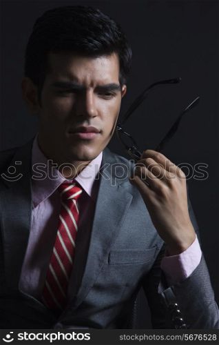 Thoughtful businessman holding glasses against black background