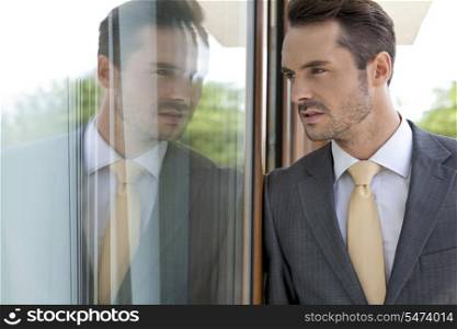 Thoughtful businessman leaning on glass door