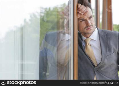 Thoughtful businessman looking away while leaning on glass door