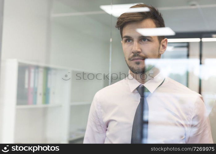 Thoughtful businessman looking through glass window at office