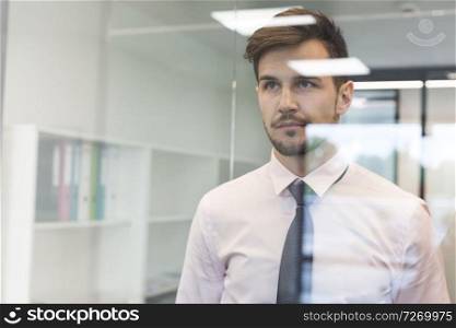 Thoughtful businessman looking through glass window at office