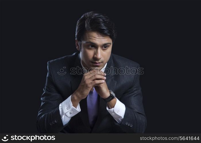Thoughtful businessman sitting with hands clasped over black background