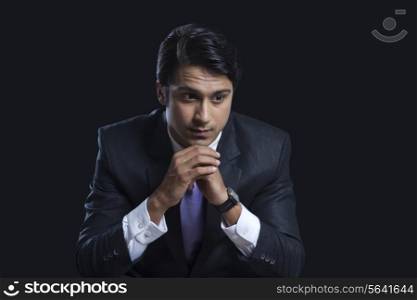 Thoughtful businessman sitting with hands clasped over black background