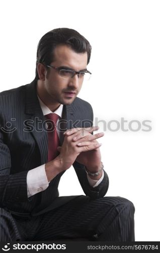 Thoughtful businessman sitting with hands clasped over white background