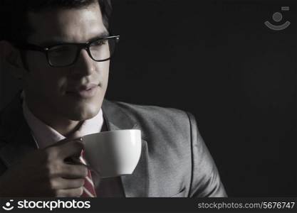Thoughtful businessman with coffee cup against black background