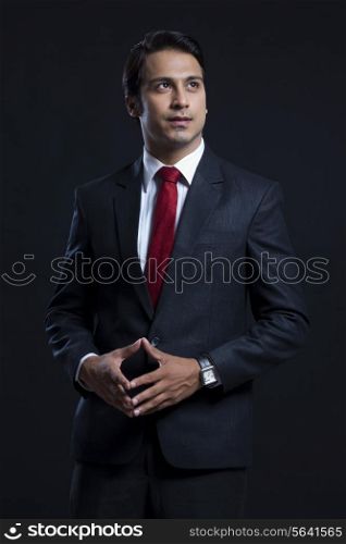 Thoughtful businessman with hands clasped standing against black background