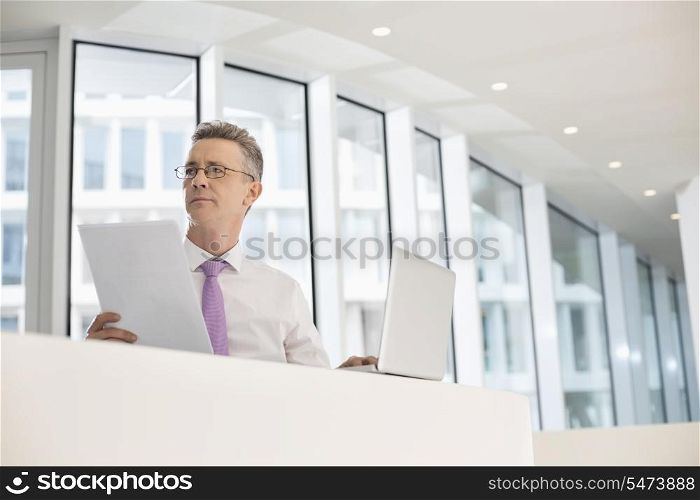 Thoughtful businessman with laptop and documents at railing