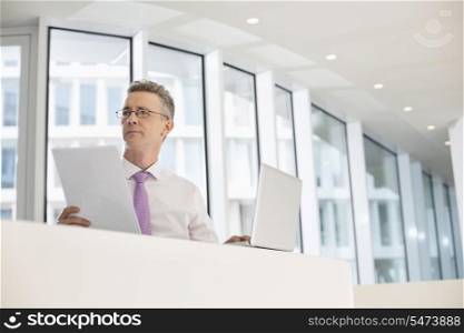 Thoughtful businessman with laptop and documents at railing