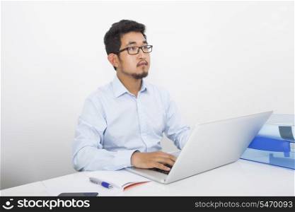 Thoughtful businessman with laptop sitting at desk in office