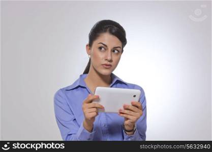 Thoughtful businesswoman holding digital tablet over gray background