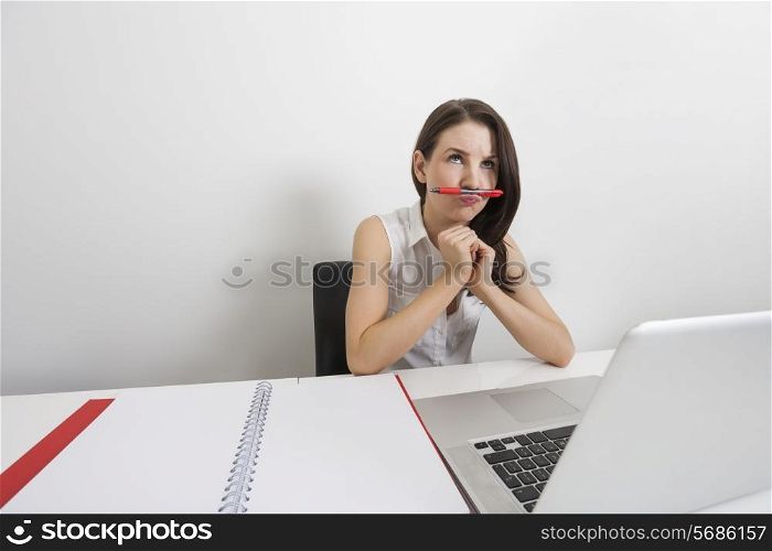 Thoughtful businesswoman holding pen under nose at desk in office