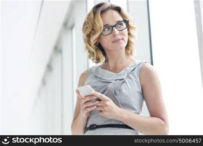 Thoughtful businesswoman holding smartphone at new office