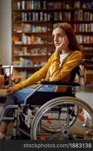 Thoughtful disabled female student in wheelchair, disability, bookshelf and university library interior on background. Handicapped young woman studying in college, paralyzed people get knowledge. Thoughtful disabled female student in wheelchair
