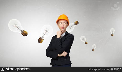 Thoughtful engineer woman. Attractive woman in helmet with hand on chin looking thoughtfully away