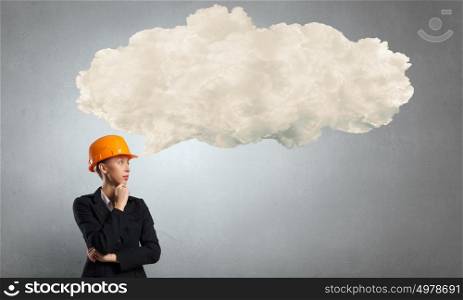 Thoughtful engineer woman. Attractive woman in helmet with hand on chin looking thoughtfully away