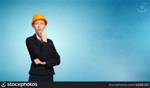 Thoughtful engineer woman. Attractive woman in helmet with hand on chin looking thoughtfully away