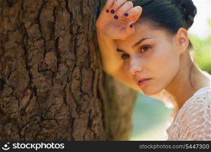 Thoughtful girl lean against tree