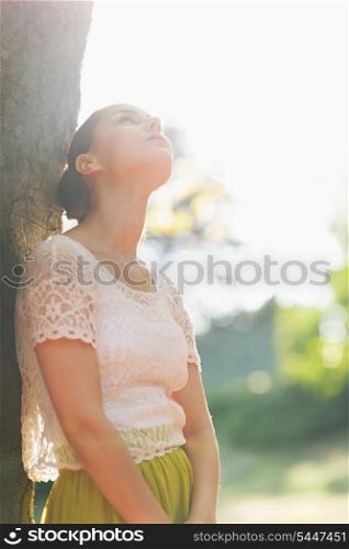 Thoughtful girl lean against tree