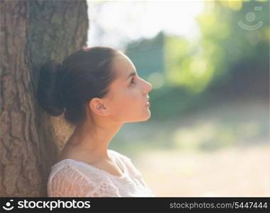 Thoughtful girl leaning on tree and looking on copy space