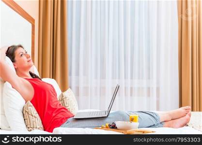 thoughtful girl with a laptop resting on a bed