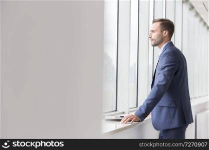 Thoughtful handsome young businessman looking through window in new office