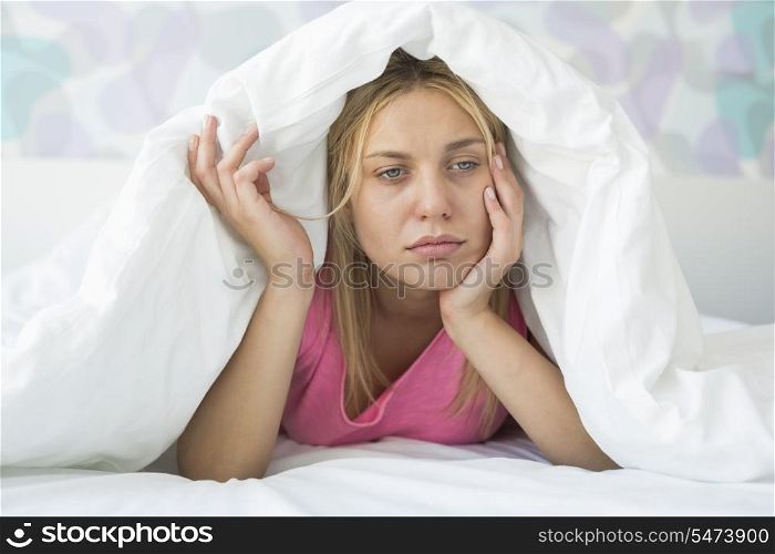 Thoughtful ill woman covered with quilt in bed