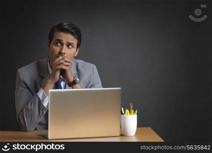 Thoughtful Indian businessman sitting with laptop at desk