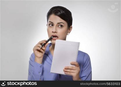 Thoughtful Indian businesswoman with notebook and pen over gray background