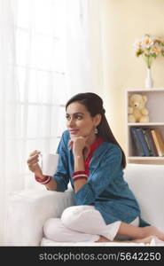 Thoughtful Indian woman having coffee in living room