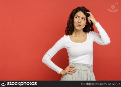 Thoughtful italian female minded thinking, creating solution planning idea looking up with hand on head and hair. Young hispanic woman pensive thinking isolated on red background on copy space.. Millennial female minded think on solution, plan or idea looking up isolated on red background