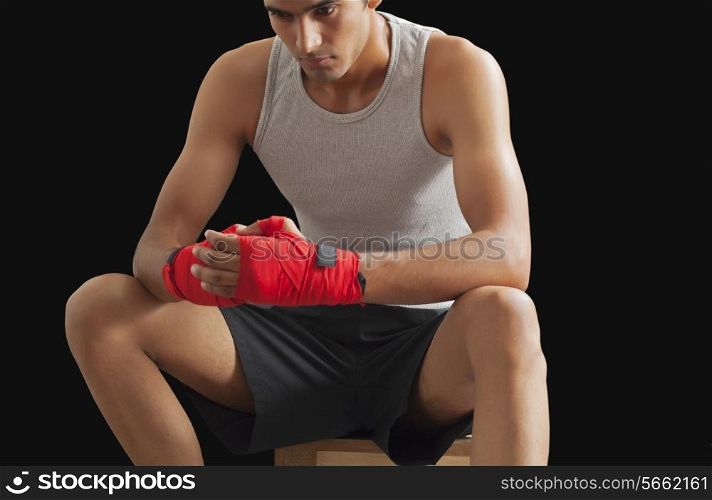 Thoughtful male boxer sitting against black background