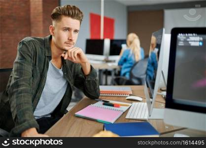 Thoughtful male IT specialist sits at the table in office. Web programmer or designer at workplace, creative occupation. Modern information technology, corporate team. Thoughtful male IT specialist sits at the table