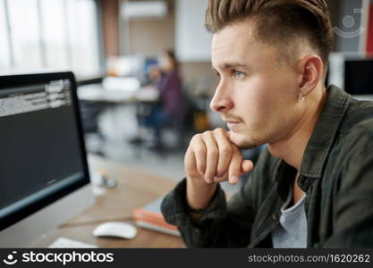 Thoughtful male IT specialist sits at the table in office. Web programmer or designer at workplace, creative occupation. Modern information technology, corporate team. Thoughtful male IT specialist sits at the table