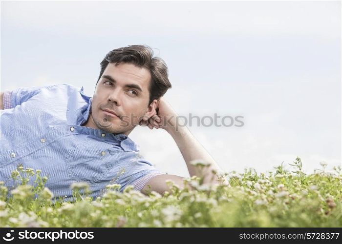 Thoughtful man lying on grass against sky