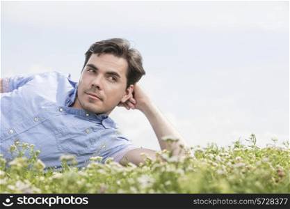 Thoughtful man lying on grass against sky