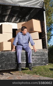 Thoughtful man sitting in the truck with pile of boxes behind him