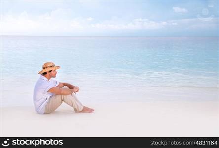Thoughtful man sitting on the beach, side view, looking away, relaxation near sea, enjoying seascape, summer holidays and vacation concept