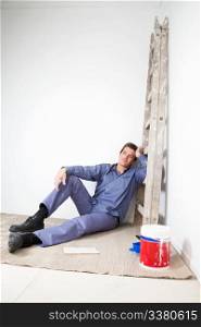 Thoughtful mature man sitting on floor with paint bucket beside