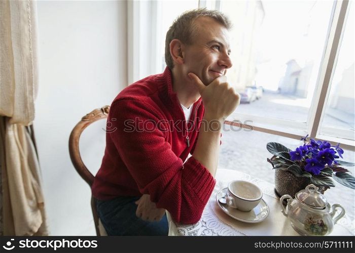 Thoughtful mid adult man sitting at table in cafe