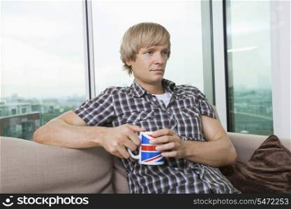 Thoughtful mid-adult man sitting with coffee cup in living room at home