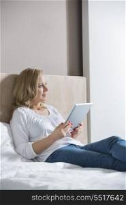 Thoughtful mid adult woman holding digital tablet in bedroom