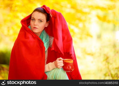 thoughtful pensive woman in autumn park relaxing enjoying hot drink coffee or tea, holding red mug with warm beverage. Yellow leaves background