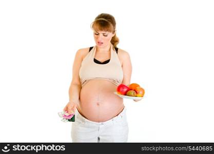Thoughtful pregnant woman making choice between pills and fruits isolated on white&#xA;