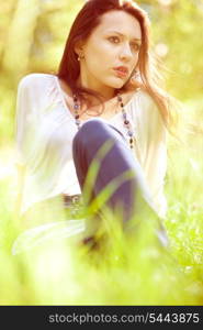 Thoughtful pretty young girl sitting on green grass&#xA;